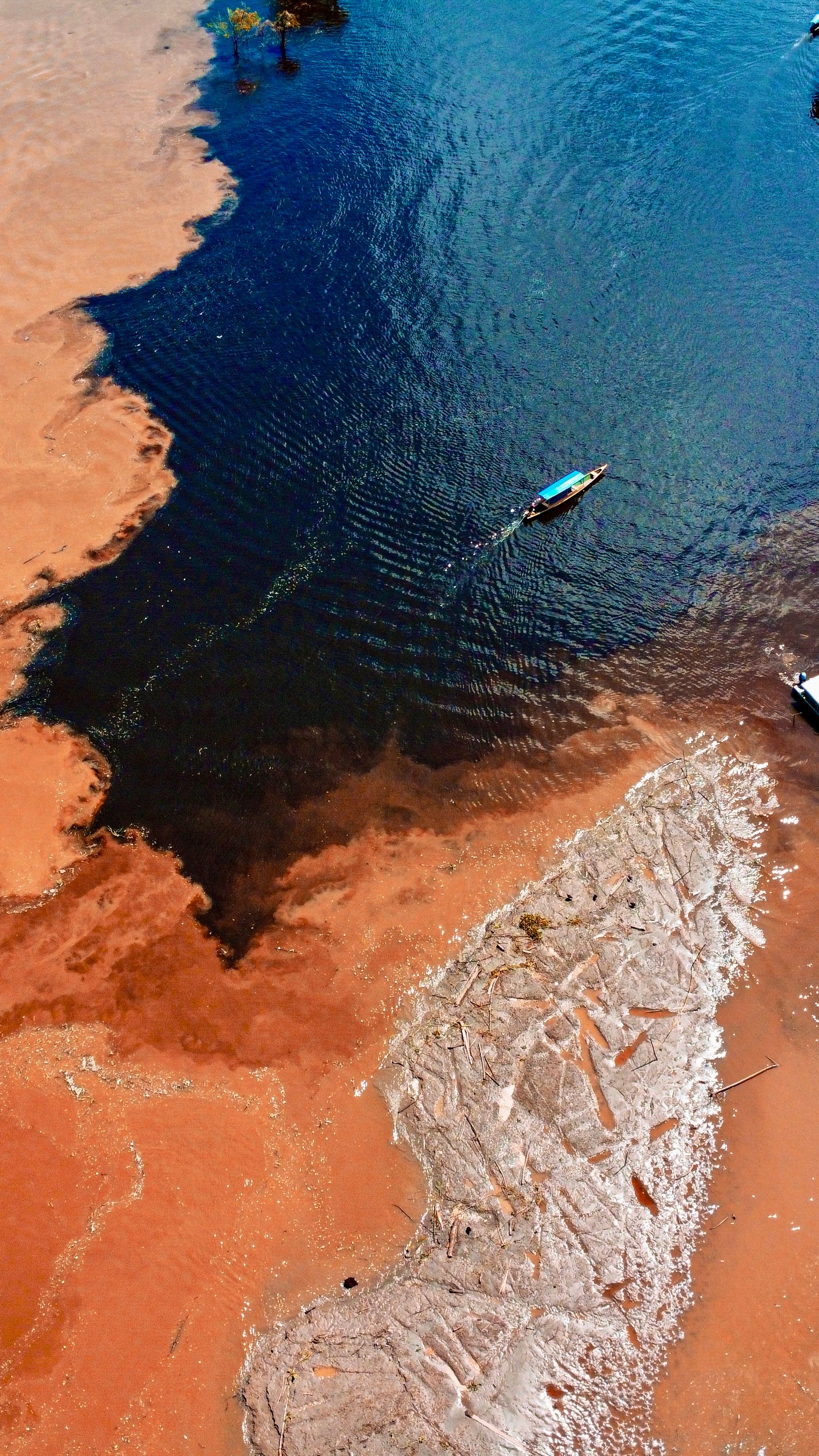 Aerial view of the Negro and Solimões rivers meeting, with a boat crossing the contrasting waters